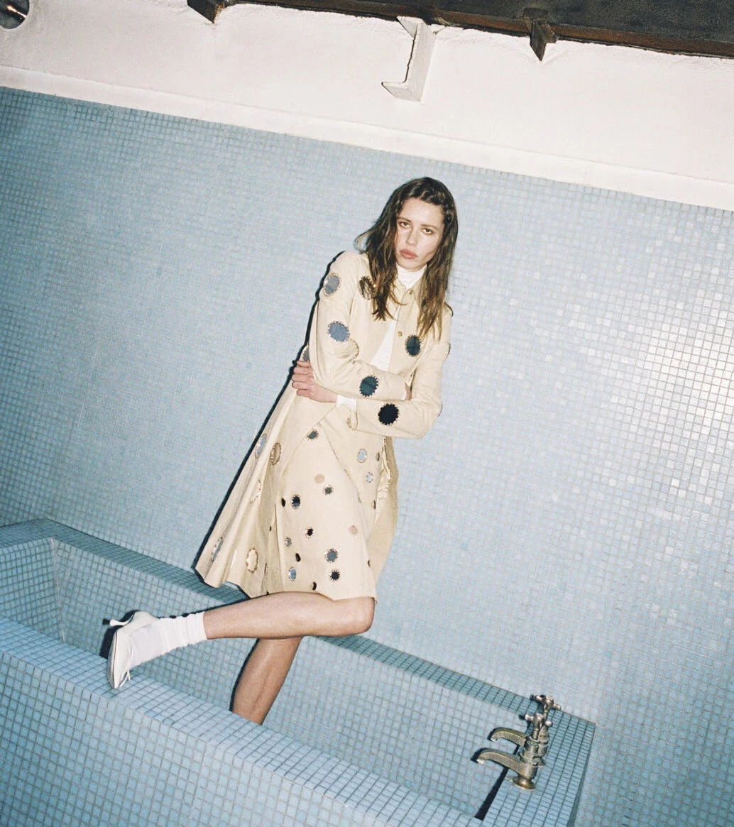 A model in a pale spotted dress against a blue tiled wall
