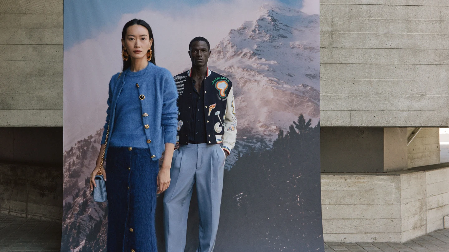 Two models in autumn layers beside a scenic studio backdrop