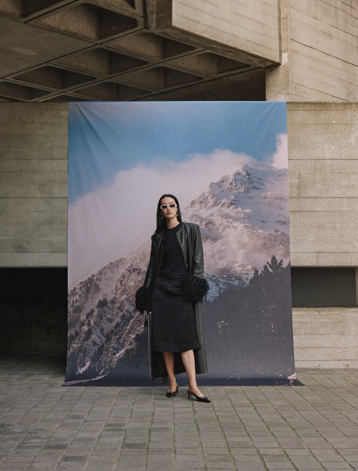 A model in a dark outfit before a mountain backdrop