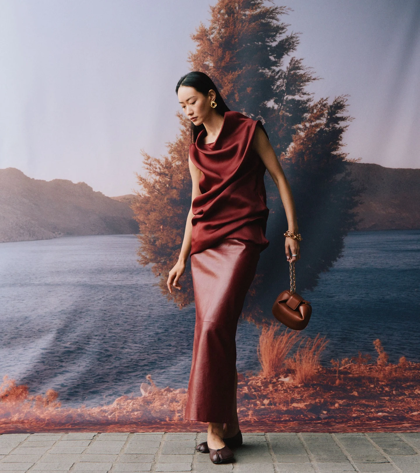 A burgundy satin outfit in front of an autumn landscape backdrop