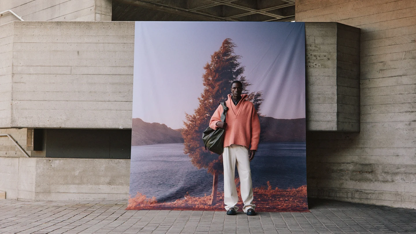 A model wearing a soft pink jacket in front of a scenic backdrop