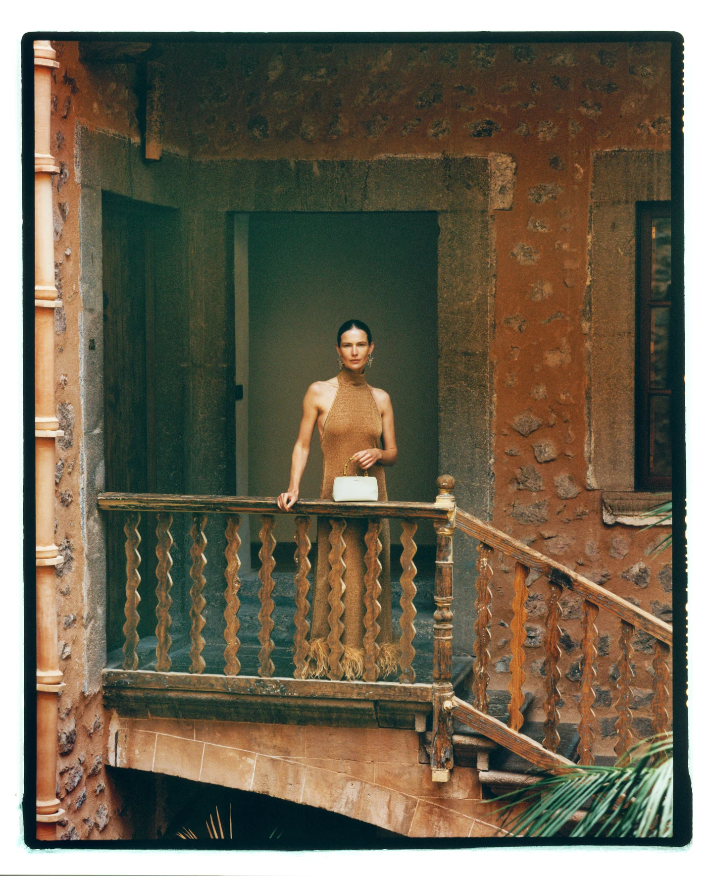 A model in a warm-toned outfit on an ornate wooden balcony