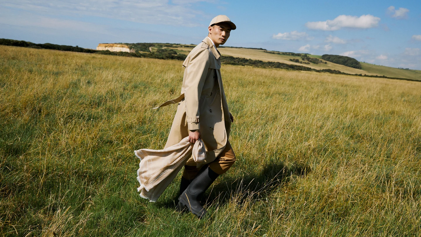 A model in a flowing coat walking through a grassy field