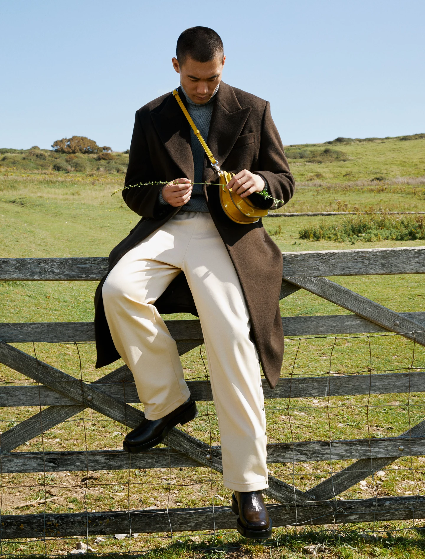 A model holding a small bag while sitting on a wooden gate