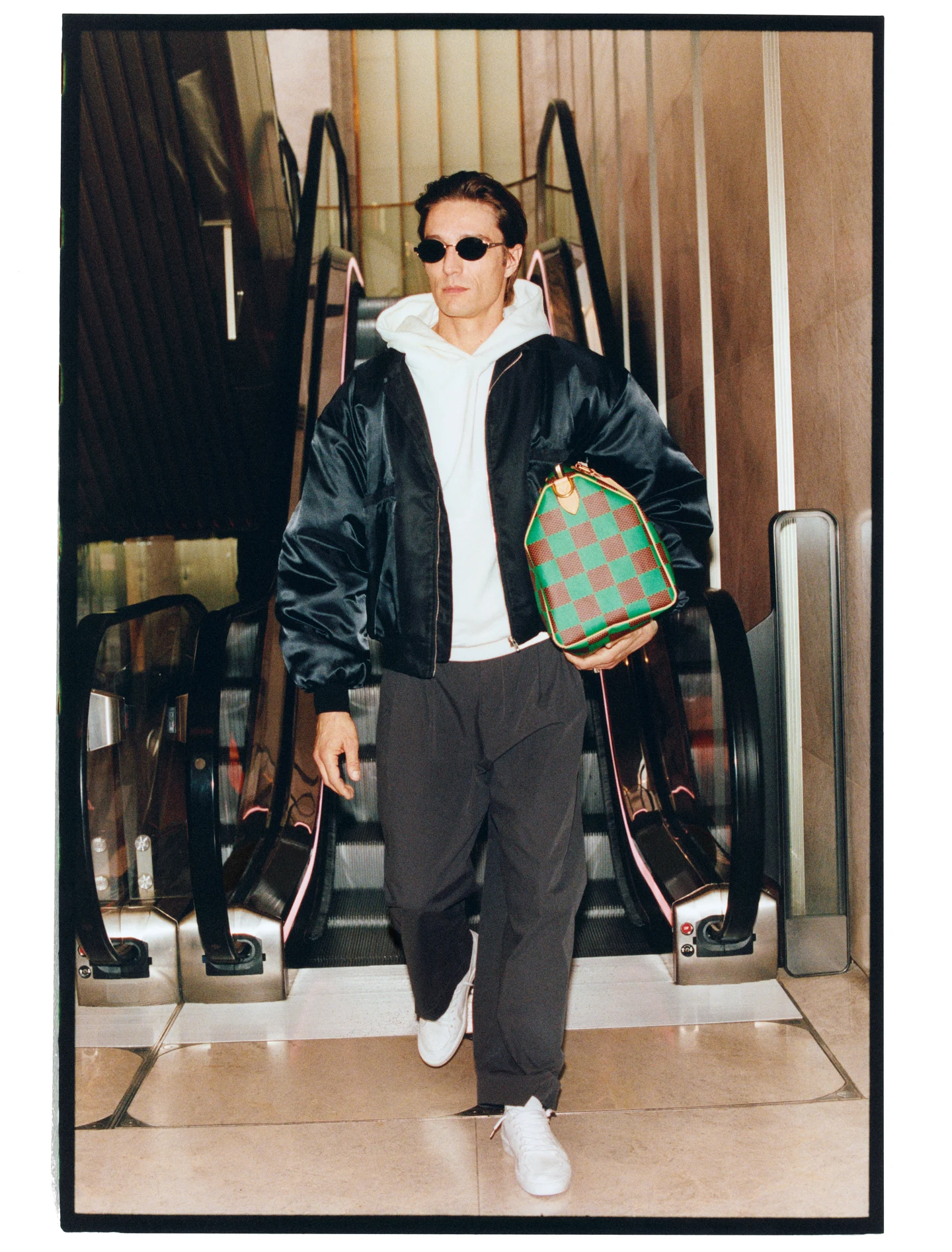 A model in a layered outfit with a green handbag